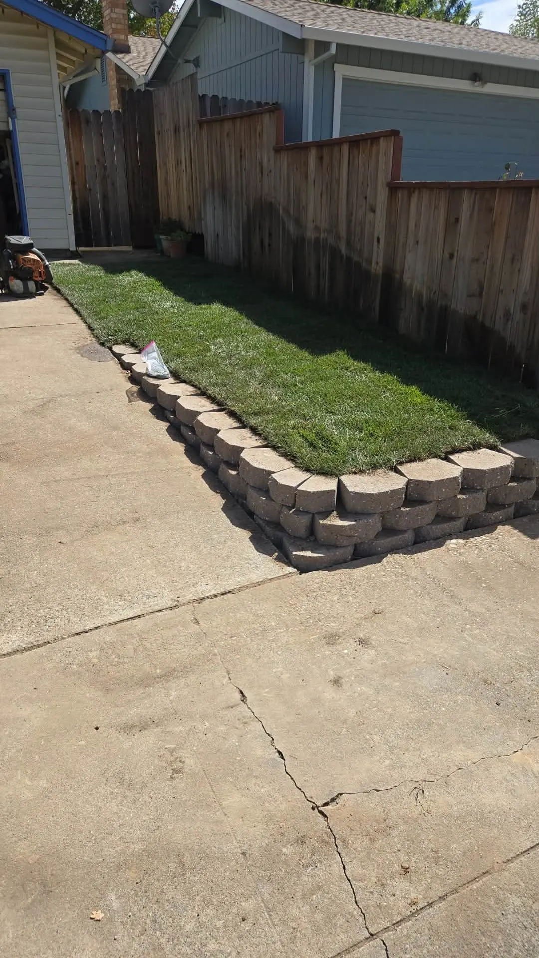 Newly graded and leveled ground with a segmental retaining wall and fresh sod along a driveway